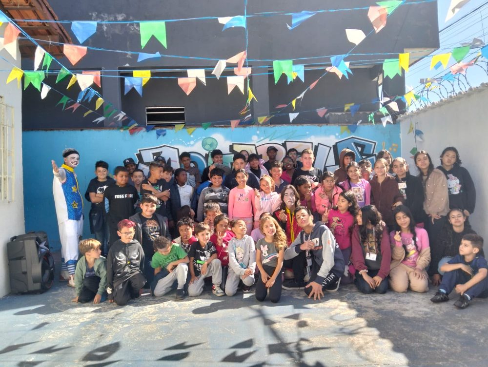 Crianças e adolescentes atendidos pela AADVIS reunidos e sorrindo em uma festa junina, com bandeirinhas coloridas ao fundo