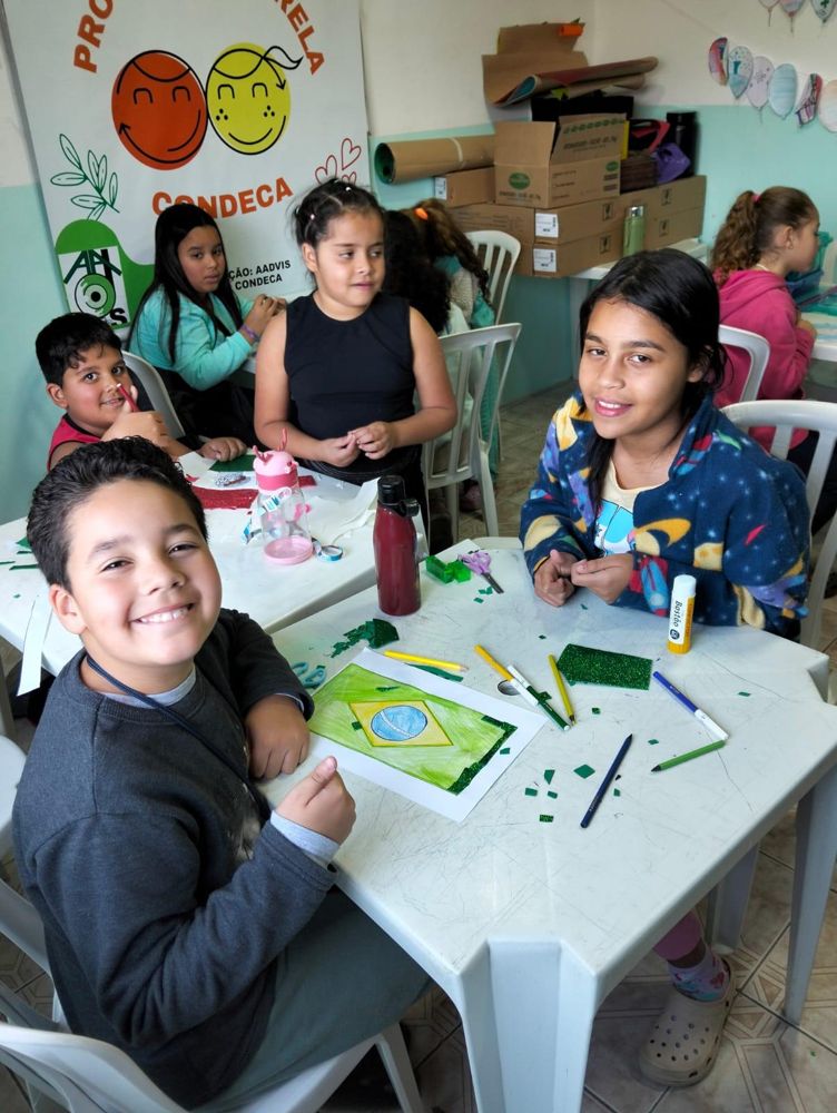 Crianças fazendo atividade de artes e colagem em mesa de oficina do projeto Aquarela