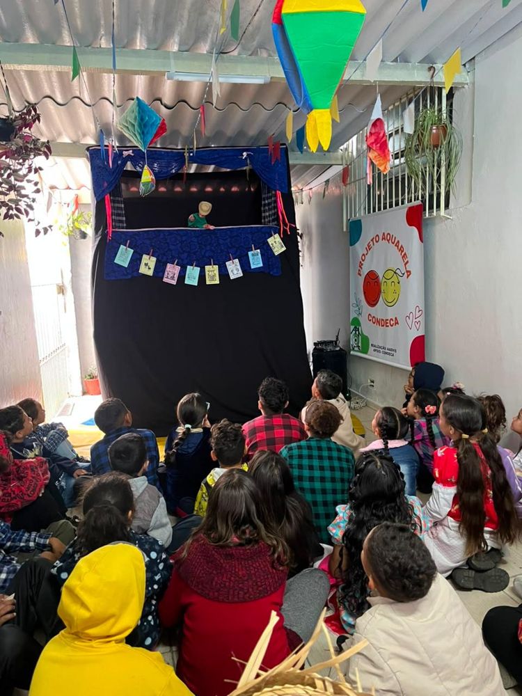 Crianças assistindo a uma apresentação de teatro de fantoches em festa junina da AADVIS